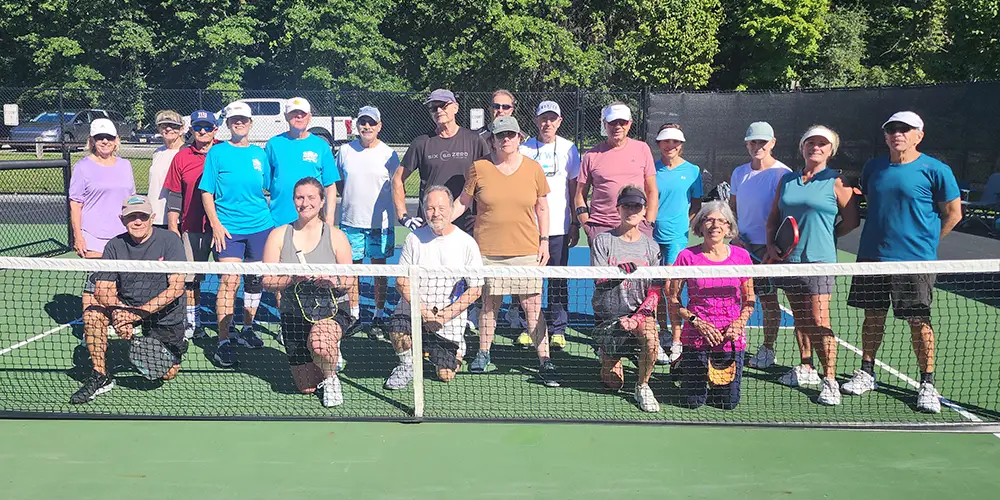 group of people posing for picture on pickleball court